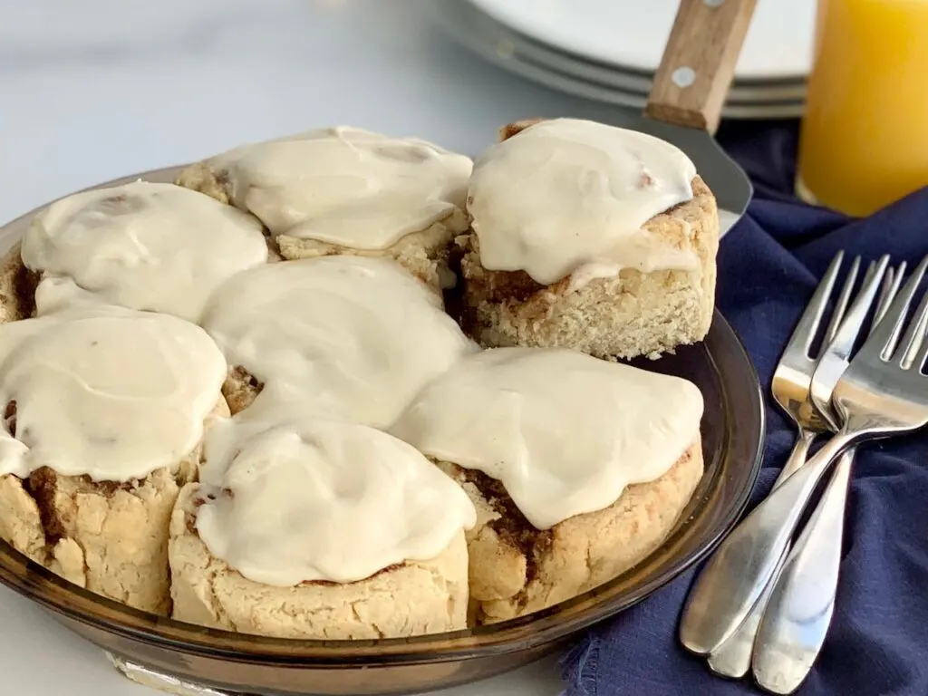 A round pie pan filled with  gooey soft cinnamon rolls with a cream cheese frosting.