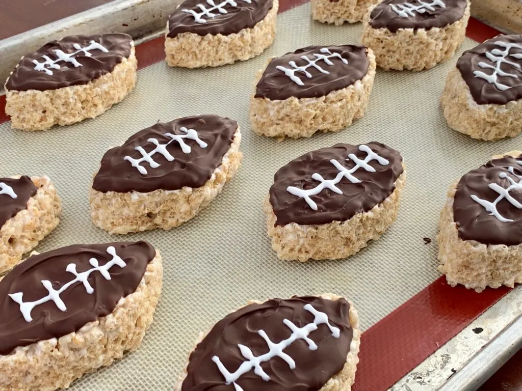 Rice krispie in the shape of a football with melted chocolate on top and white icing to looking like a football.