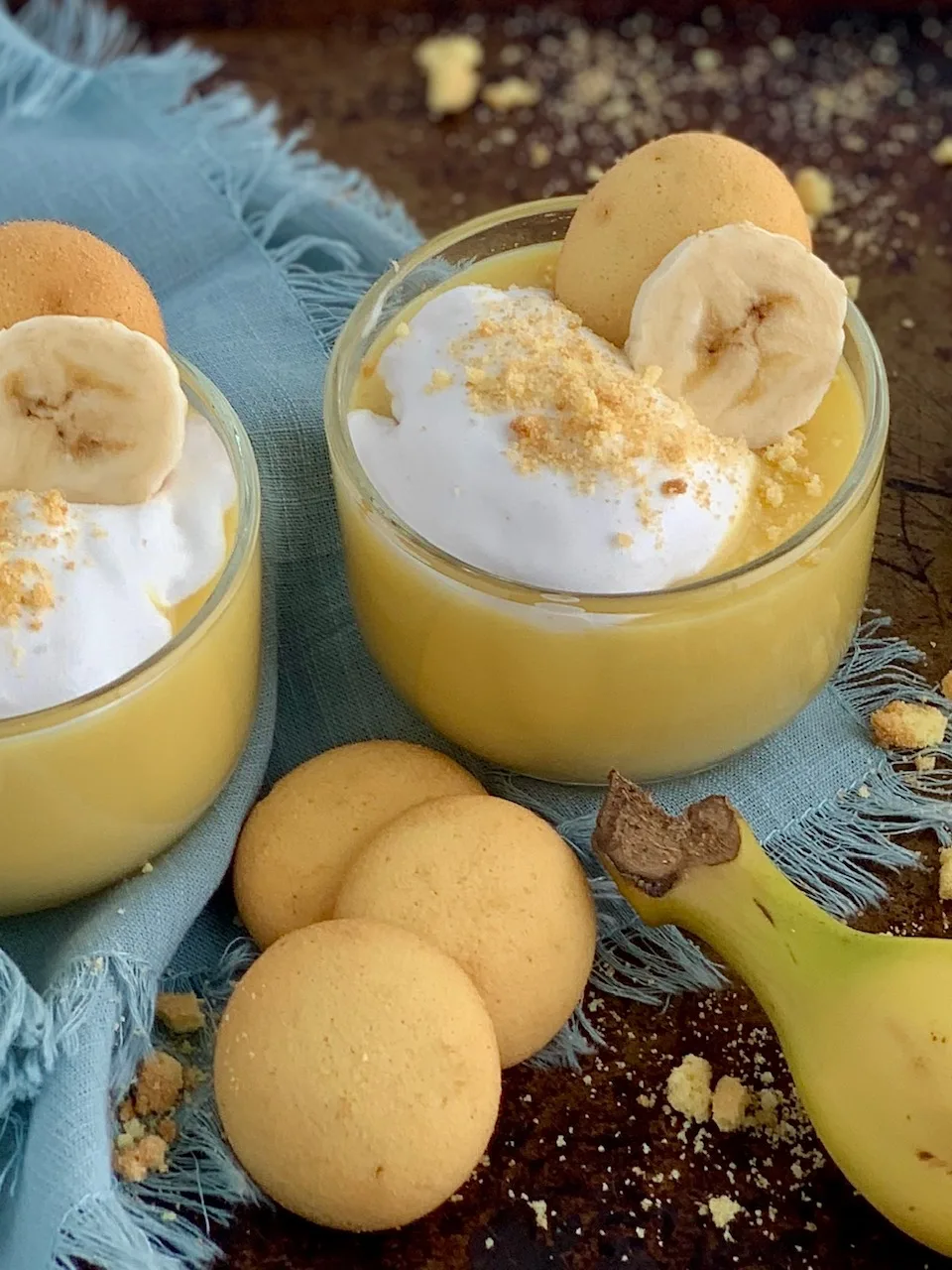 2 mini dessert glasses filled with layers of sliced bananas, vanilla wafer cookies, banana pudding, and creamy whipped topping. Then cookie crumbs, another cookie, and a banana slice on top of that.