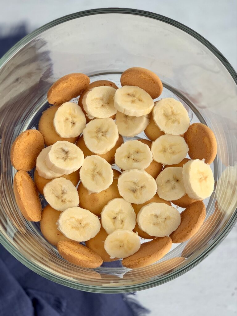 A glass trifle bowl filled with layers of vanilla wafer cookies and sliced bananas.