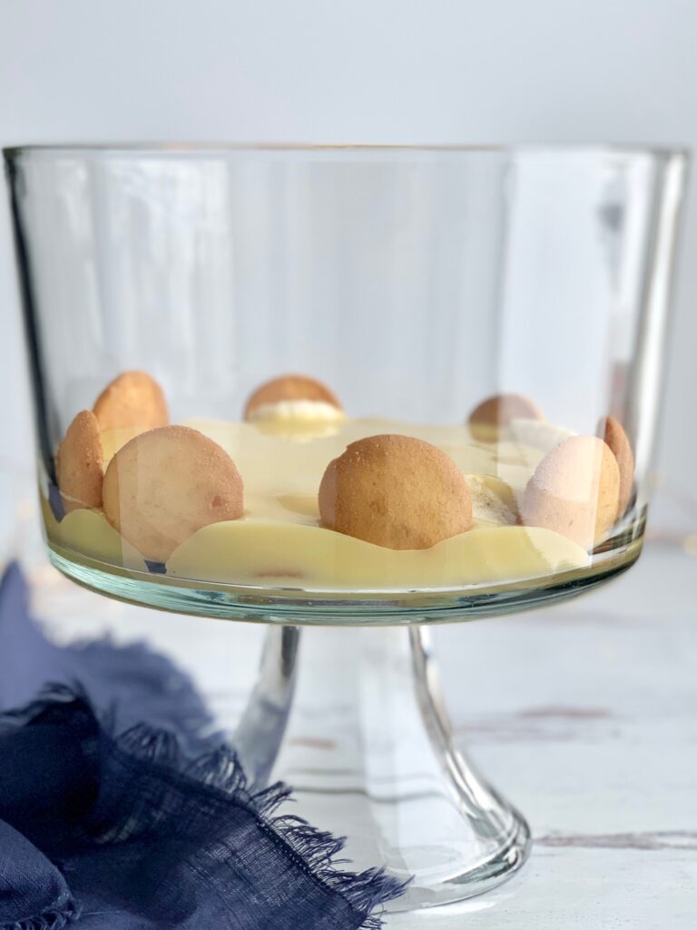 A glass trifle bowl filled with layers of vanilla wafer cookies, sliced bananas, vanilla pudding.