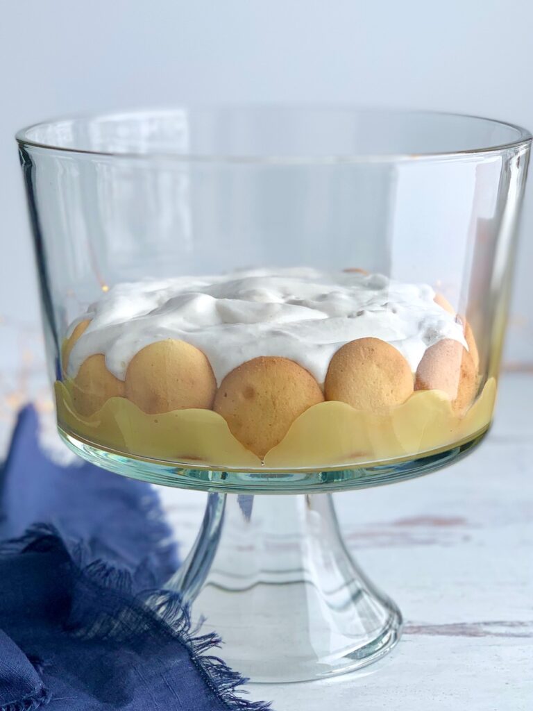 A glass trifle bowl filled with layers of vanilla wafer cookies, sliced bananas, vanilla pudding, creamy whipped topping.