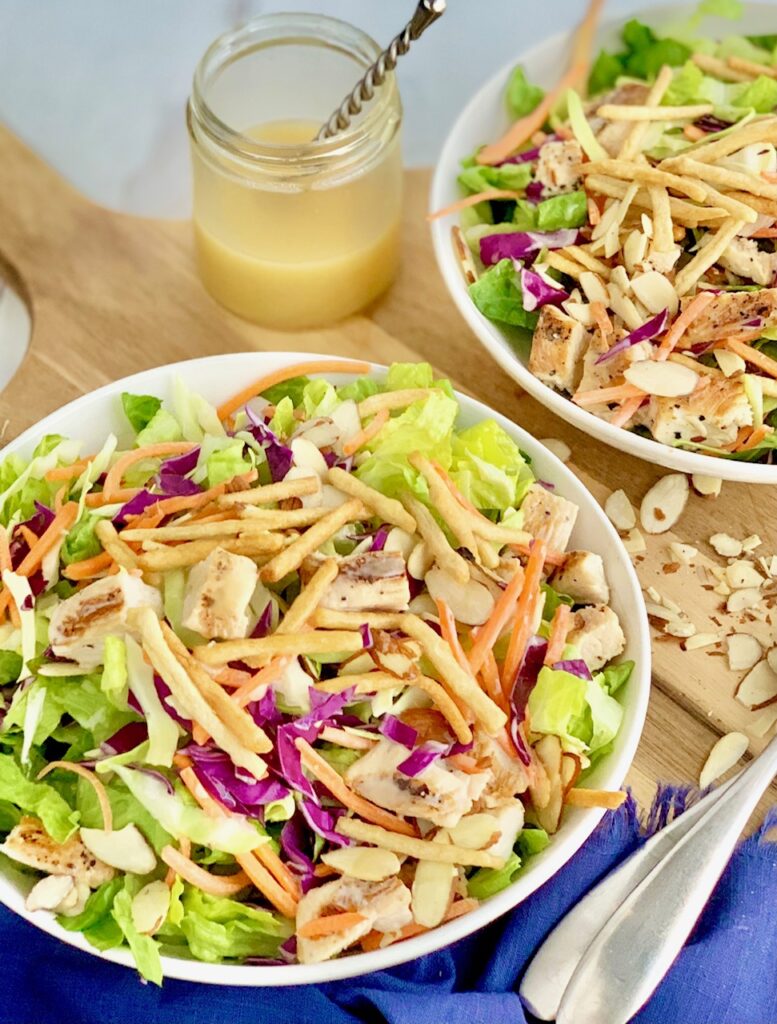 2 small salad serving plates with cuts of romaine lettuce, purple cabbage, light green napa cabbage, chunks of grilled chicken, shredded carrots, and lots of sliced almonds. There is even a few strips of wonton strips.