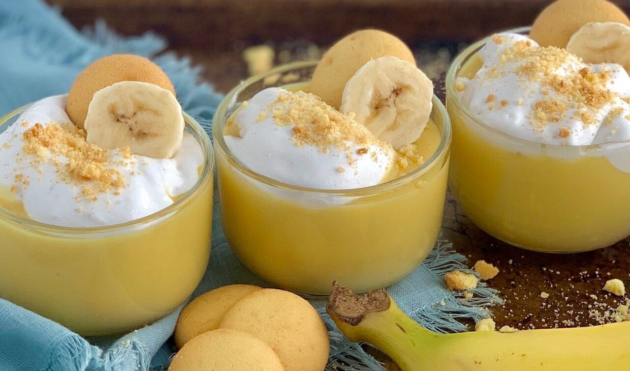 3 mini dessert glasses filled with layers of sliced bananas, vanilla wafer cookies, banana pudding, and creamy whipped topping. Then cookie crumbs, another cookie, and a banana slice on top of that.