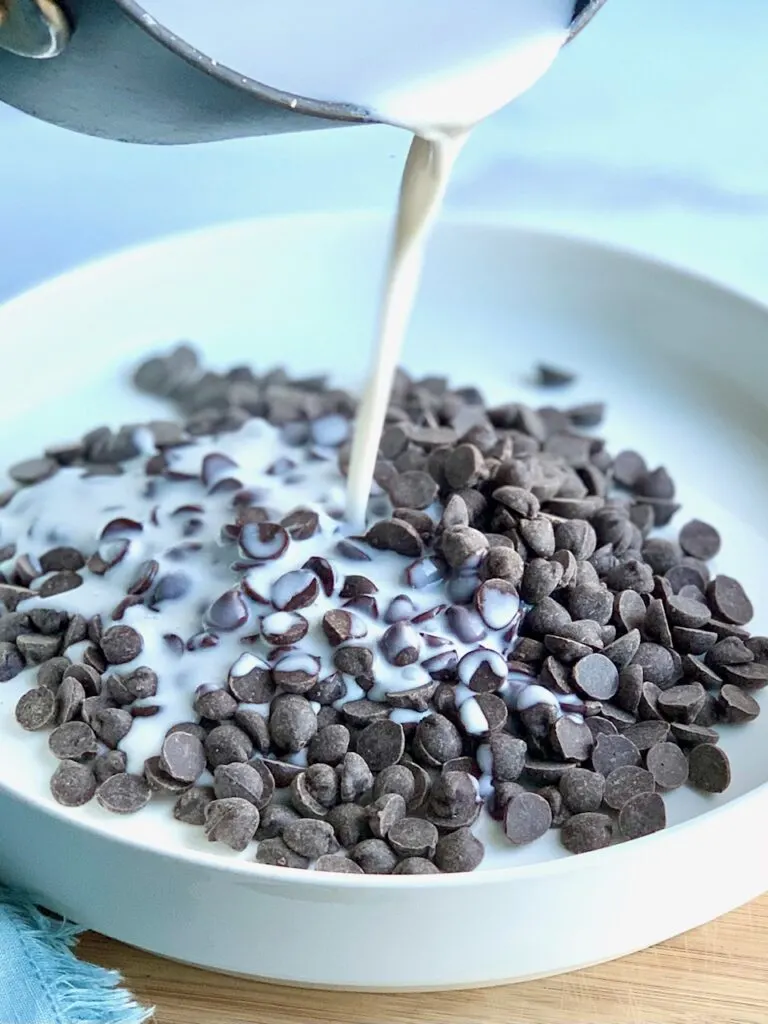 Heated coconut cream being poured on a platter of dark chocolate morsels.