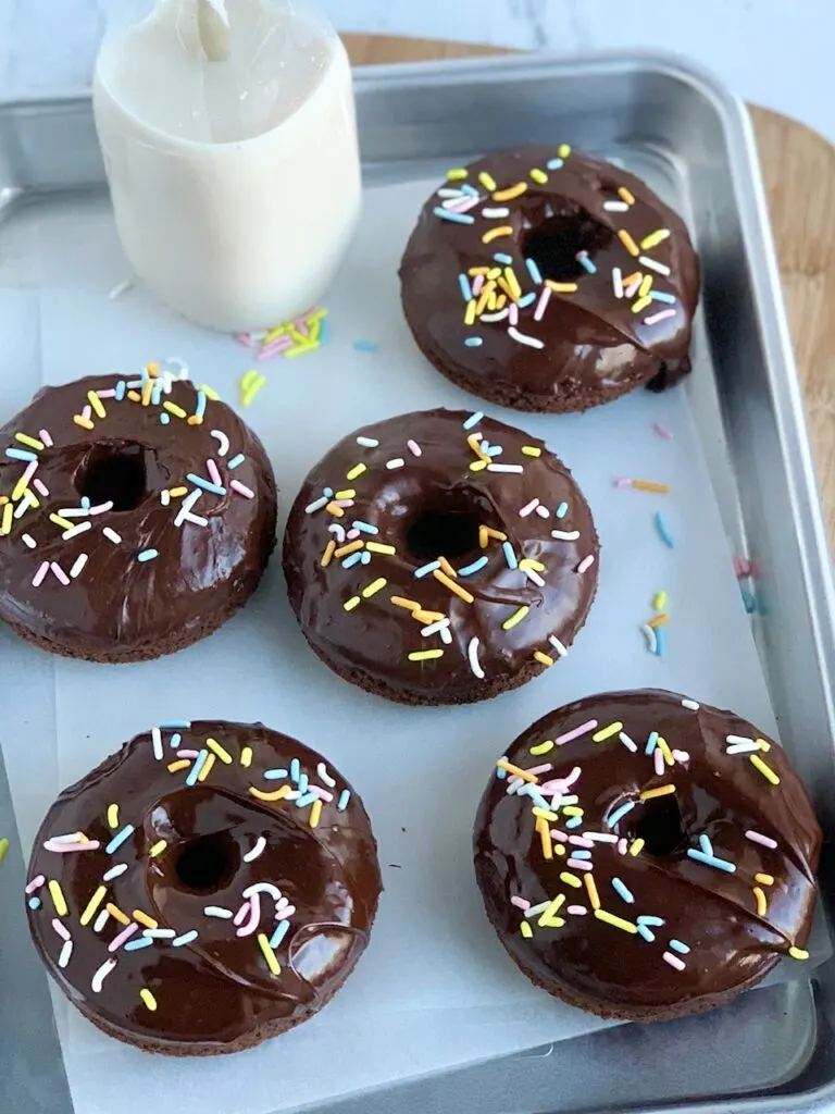 A tray of 5 chocolate donuts after they've been dipped in chocolate ganache frosting and topped with festive Easter colored sprinkles. 