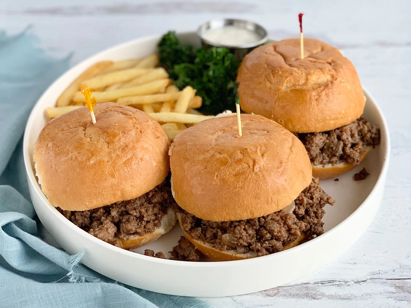A white platter full of a meat mixture between hamburger buns with French fries.