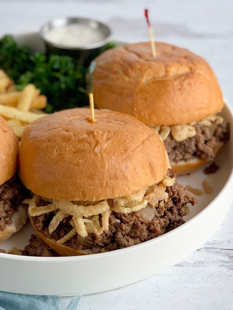 A white platter full of a meat mixture between hamburger buns with French fries.