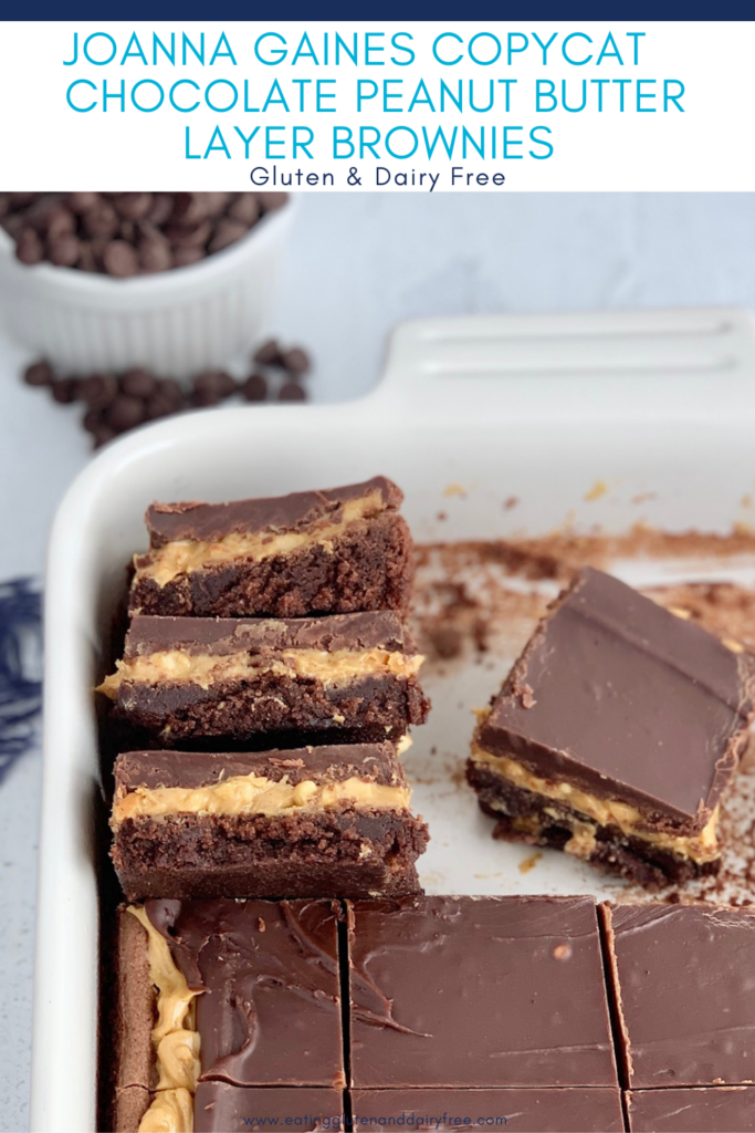 A stack of 3 cut bars. The first layer of the bars is a chocolate brownie, with crunchy peanut butter slathered over it, then topped with a soft chocolate marshmallow mixture in a baking pan with more cut bars.