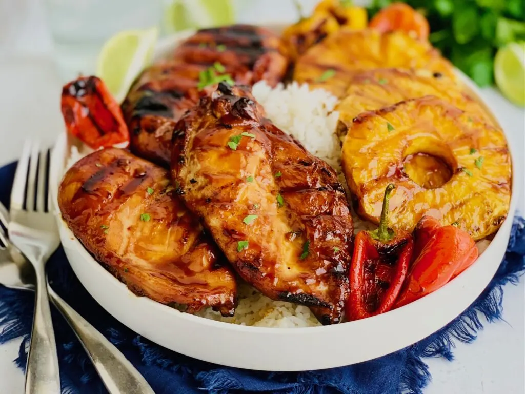 A large serving platter with jasmine rice, grilled chicken, pineapple slices, and min sweet peppers.