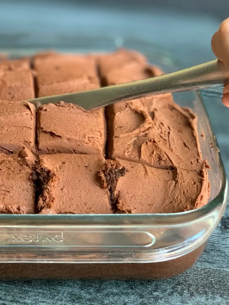 A knife cutting through a chocolate frosted  cake.