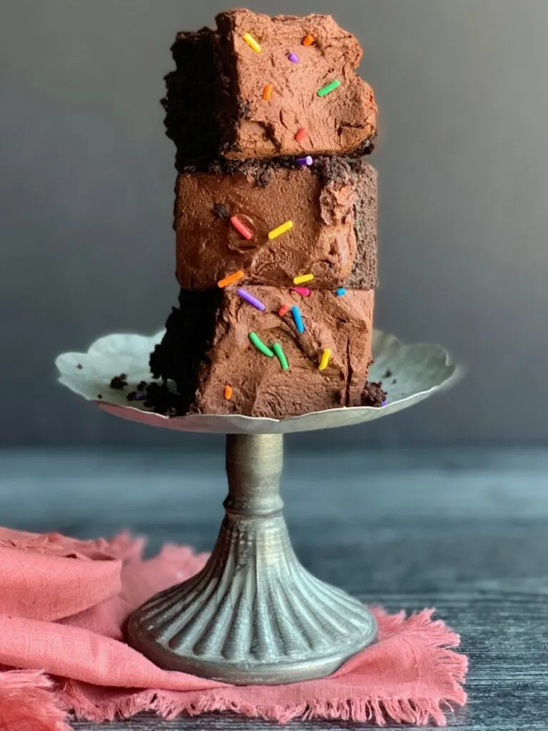 3 cut pieces of chocolate cake frosting with chocolate buttercream frosting and topped with sprinkles are stacked on top of each other.