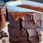 A stack of 4 slices of moist looking chocolate loaf slices with a dollop of chocolate ganache frosting dripping down from the top slice.