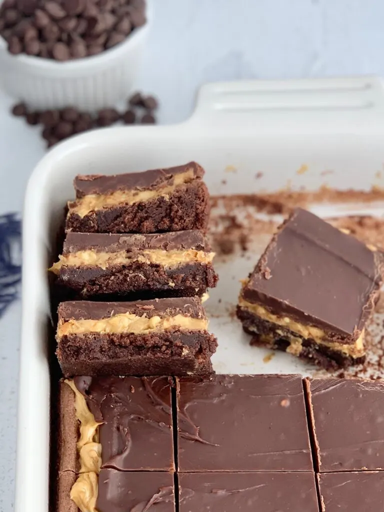 A white baking pan showing 3 bars layer on top of each other. The first layer has a brownie crust followed by crunchy peanut butter and a top layer with melted chocolate and marshmallows. 