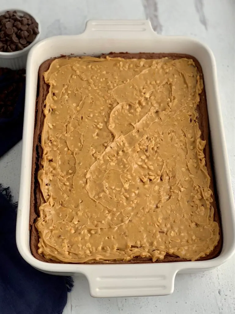 A baked chocolate brownie mix in a white 9X13-inch baking pan with crunchy peanut butter over the cooled brownie.