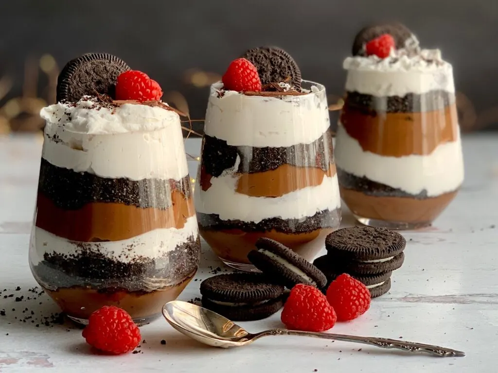 3 large dessert cups filled with layers of creamy chocolate pudding, oreo like cookie crumbs, and cocowhip topped with a raspberry.