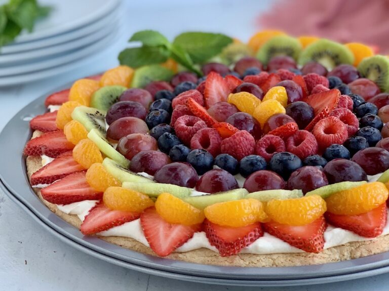 A round sugar cookie in a pizza pan with a cream cheese mixture spread on it. Then it's topped with fresh sliced fruit such as strawberries, kiwi, grapes, and raspberries.,
