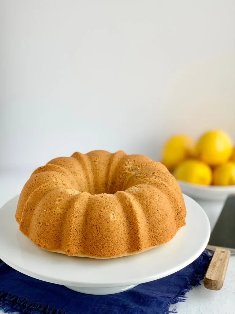 A lemon bunt cake without frosting sitting on a large white cake plate.