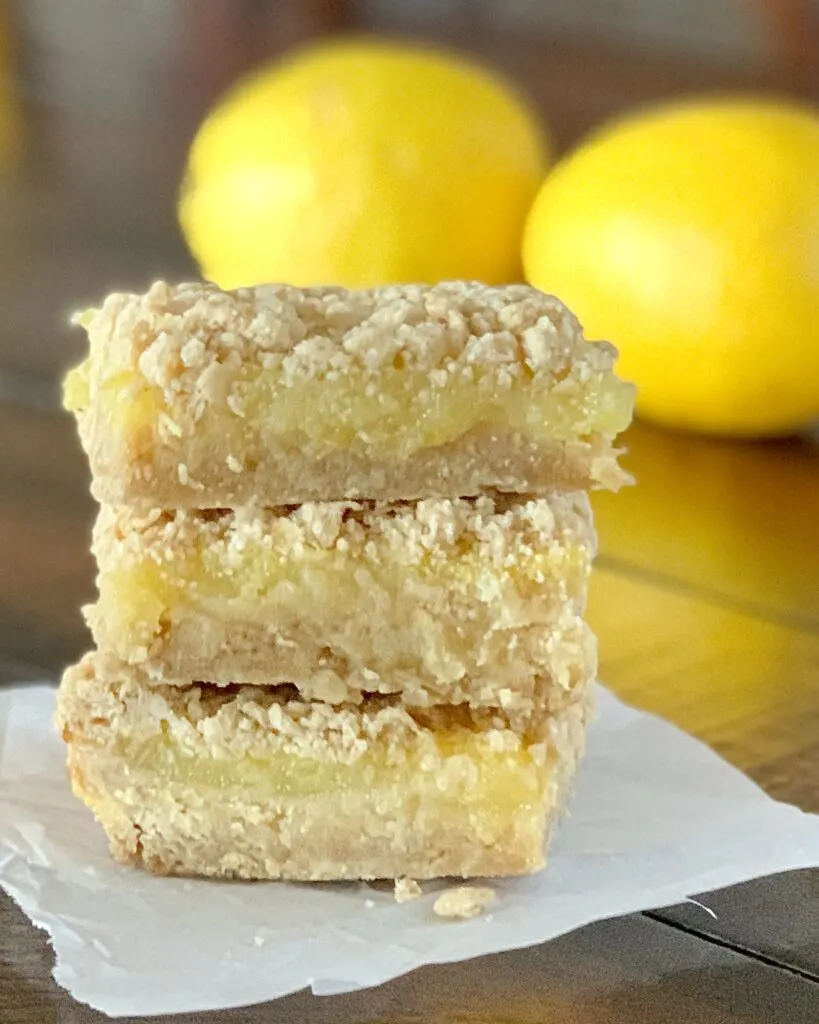 3 lemon bars stacked 
on top of each other. Each bar has a thick crust followed by a lemon filling and then topped with a streusel.
