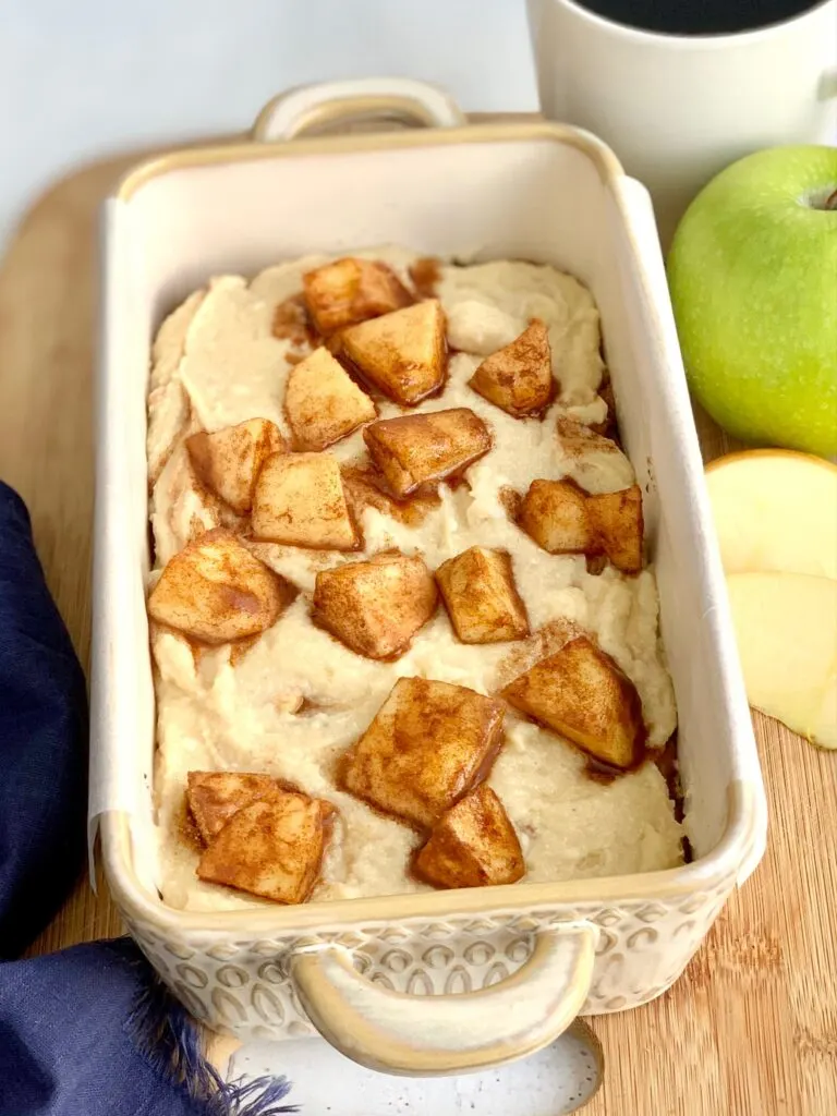 A loaf pan full of batter topped with apple chunks covered in cinnamon and sugar.