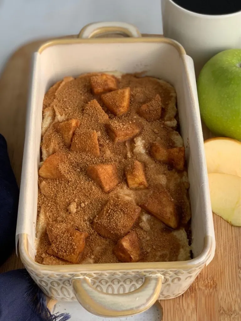 A loaf pan full of batter topped with apple chunks covered in cinnamon and sugar and topped with another layer of cinnamon and sugar.