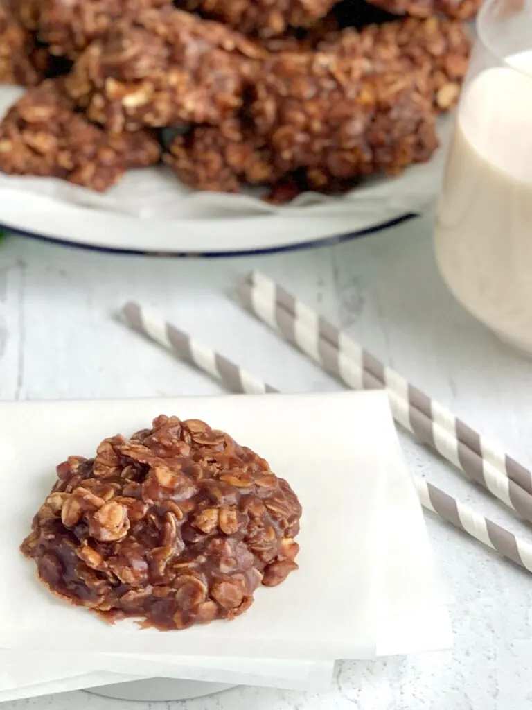 A close up of a No Bake Cookie with chocolate and peanut butter over oats next to a glass of milk and 3 drinking straws.