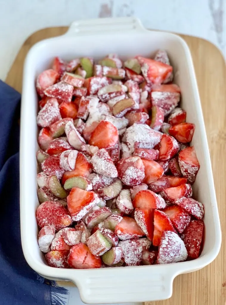 A white baking dish filled with diced fresh rhubarb and strawberries with a thick sweet juices over it.