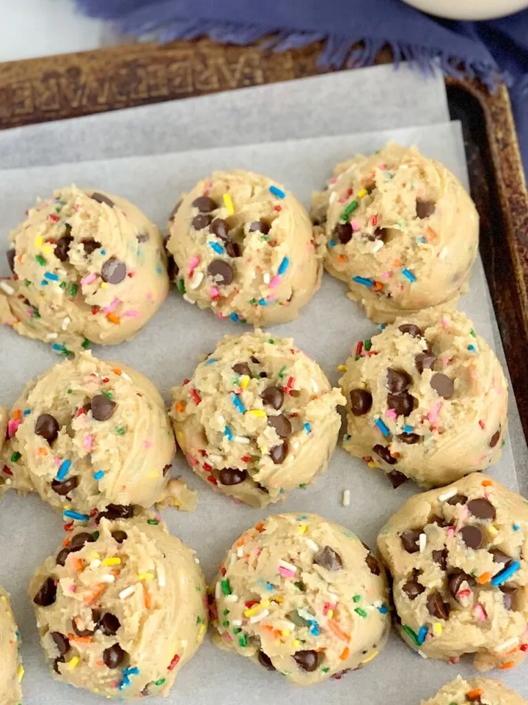 A baking sheet full of round raw dough balls of chocolate chip cookie dough with colorful sprinkles.