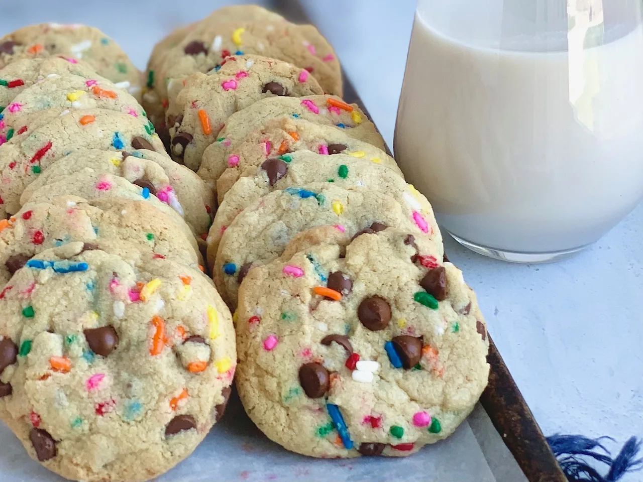 A baking sheet full of chocolate cookies with sprinkles next to a glass of dairy free milk.