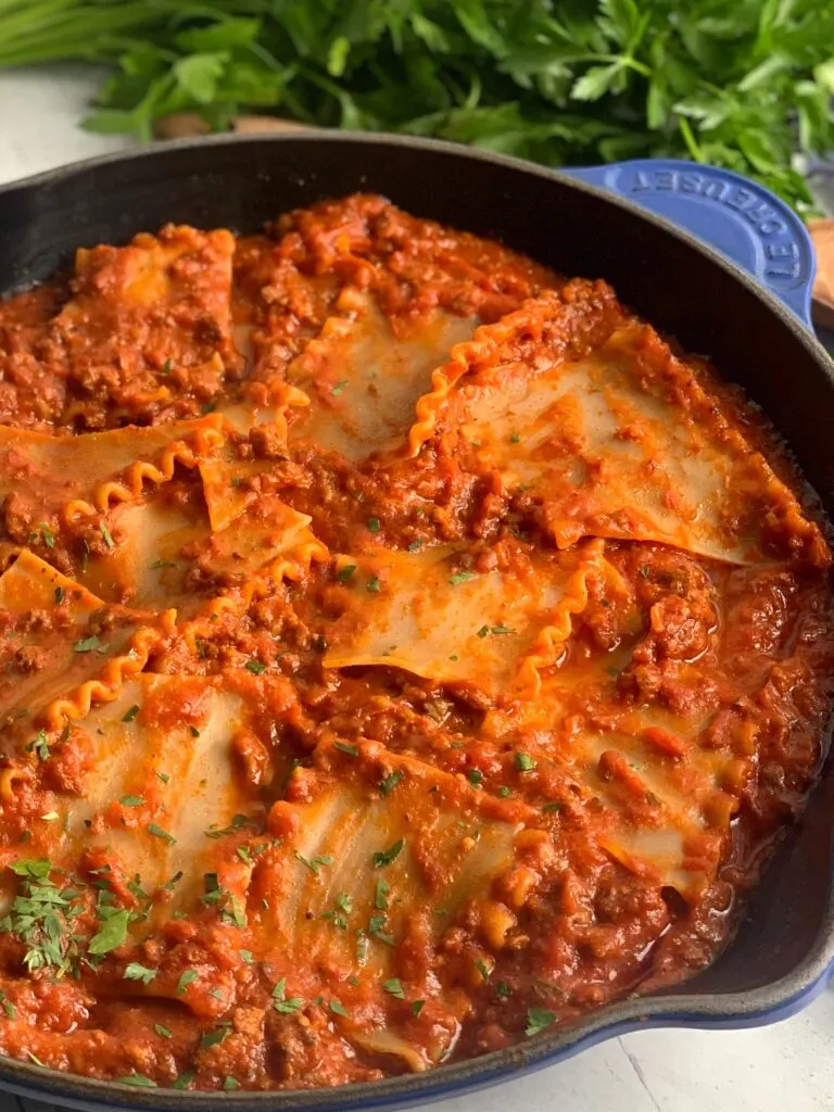 A skillet filled with tender lasagna noodles broken into pieces in a meaty marinara sauce and pieces of fresh parsley over the top.