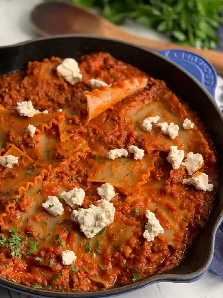 A skillet filled with tender lasagna noodles broken into pieces in a meaty marinara sauce and pieces of ricotta over the top.