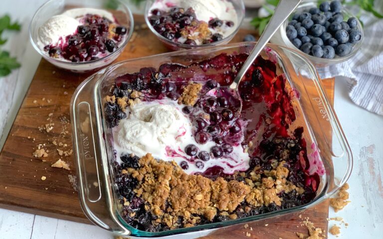 A glass baking dish filled with a thick blueberry mixture on the bottom and a golden oat, flour, butter mixture on top. There are also bowl in the background filled with the mixture.