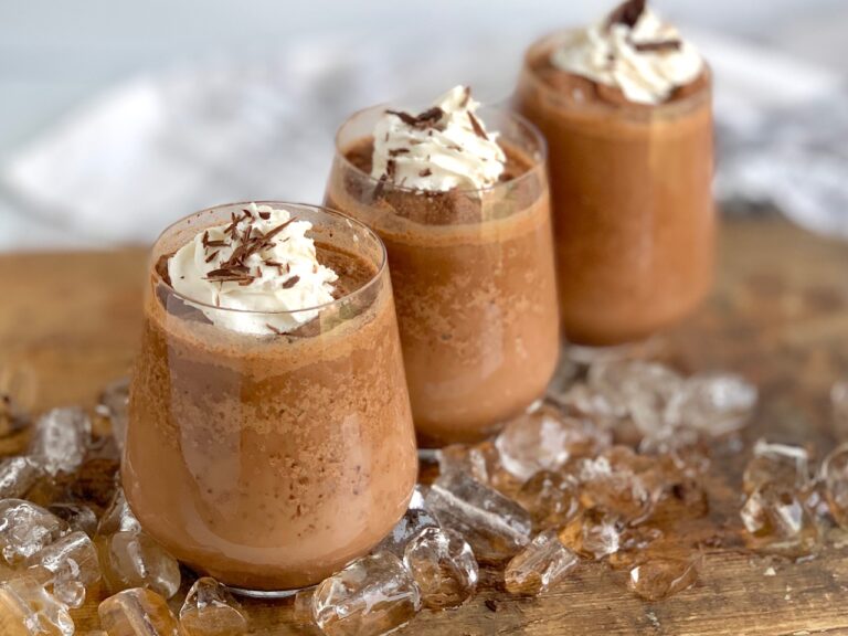 3 clear glasses filled to the brim with a slushy hot chocolate mixture and topped with swirls of whipped cream and chocolate shavings.