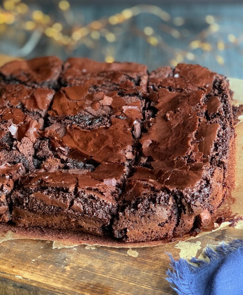 An 8x8-inch square baked brownie cut into 12 slices on a cutting board with twinkle lights in the background.