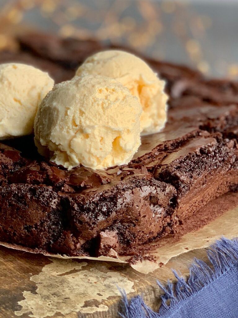 An 8x8-inch square baked brownie cut into 12 slices on a cutting board and 3 dollops of ice cream on top.