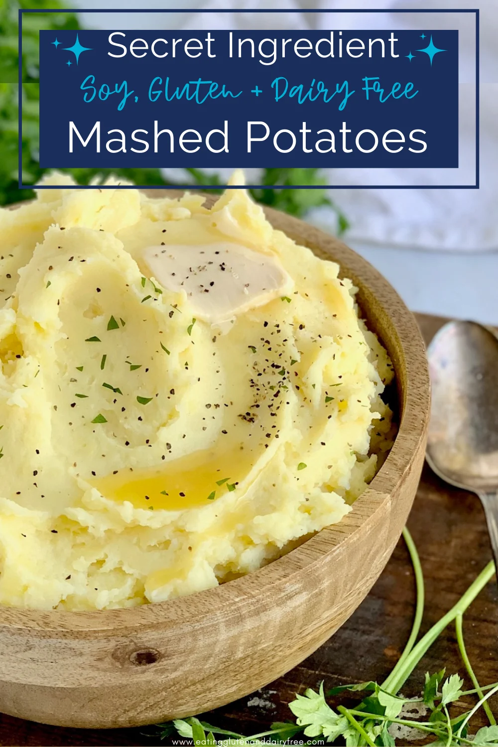 A large wooden bowl filled with creamy mashed potatoes topped with salt, pepper, melted butter and little pieces of parsley.