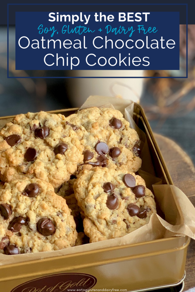 A gold colored cookie tin packed full of golden brown cookies loaded with chocolate chips next to a cup of milk.