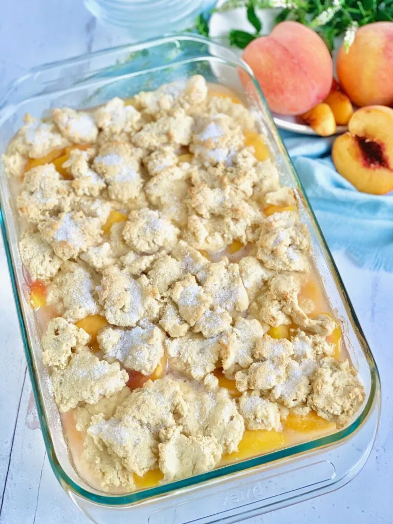 A 9x13-inch baking dish filled with a thick sweet peach mixture and topped with a biscuit-like golden brown dough. 