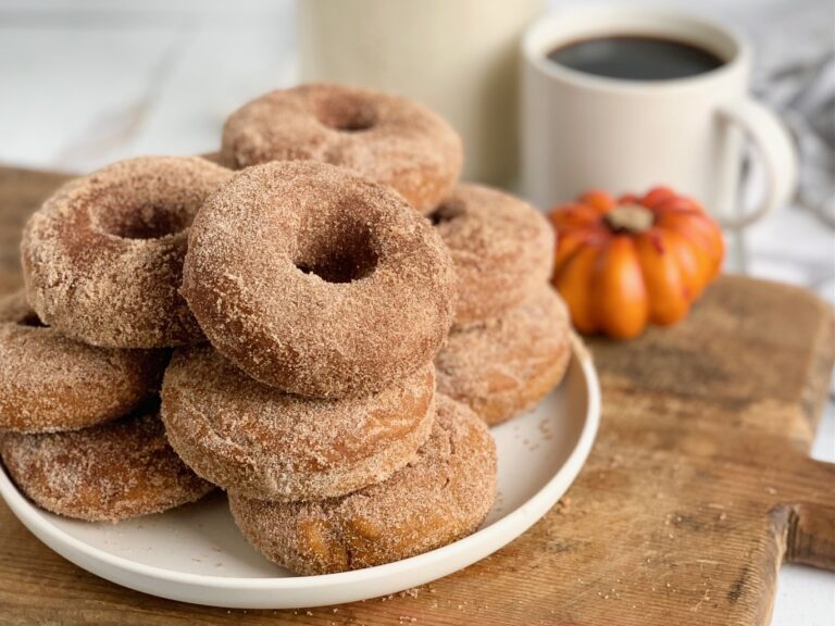 A white plate loaded with several pumpkin donuts covered with cinnamon sugar.