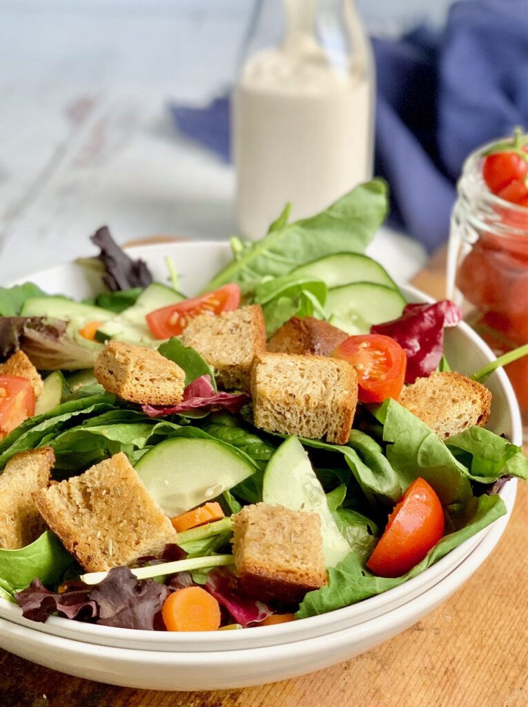 A large bowl filled with crisp greens, sliced cucumbers and grape tomatoes, and topped with buttery croutons.