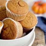 A white bowl full of pumpkin colored muffins in white muffins liners.