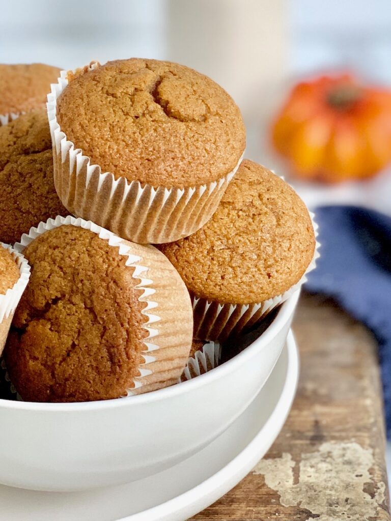 Pumpkin colored muffins in white muffins in a large white bowl.