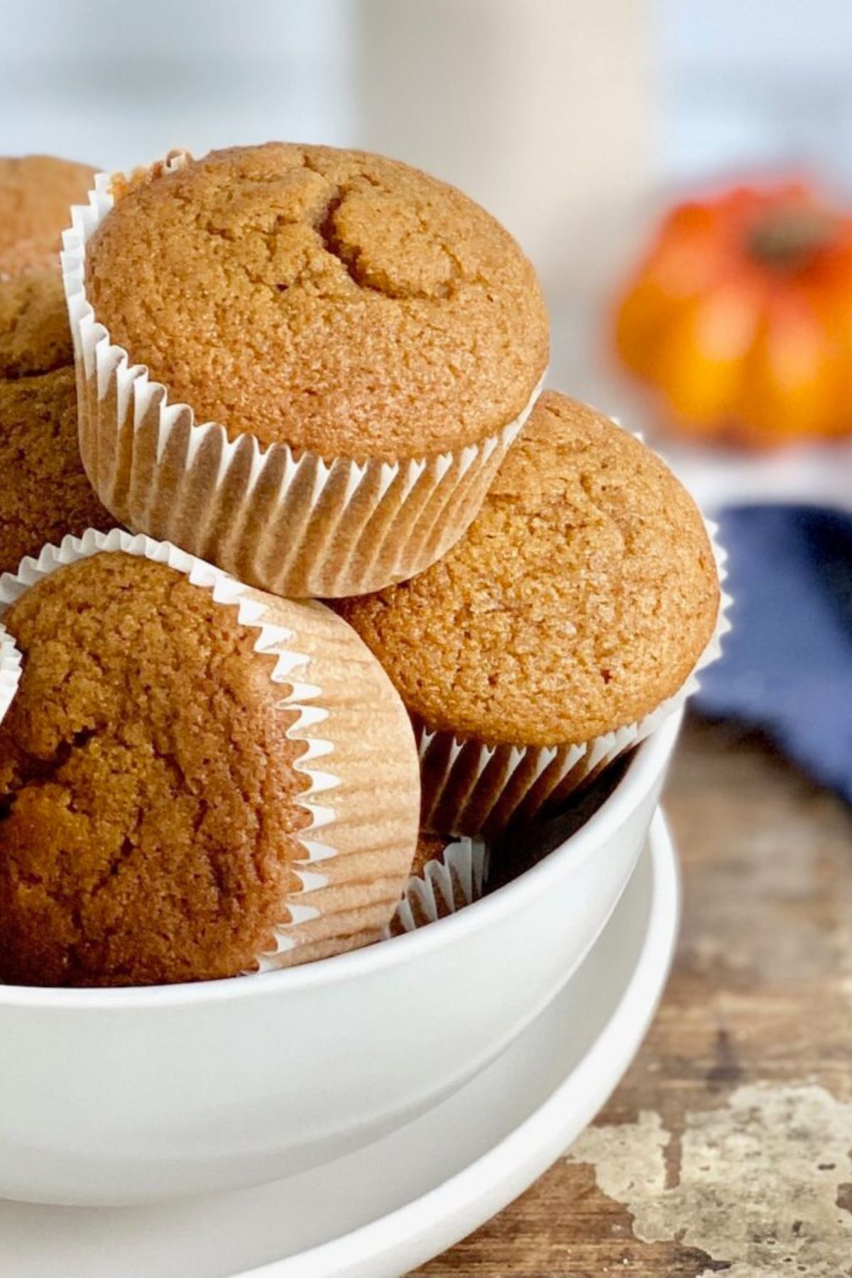 A white bowl full of pumpkin colored muffins in white muffins liners.