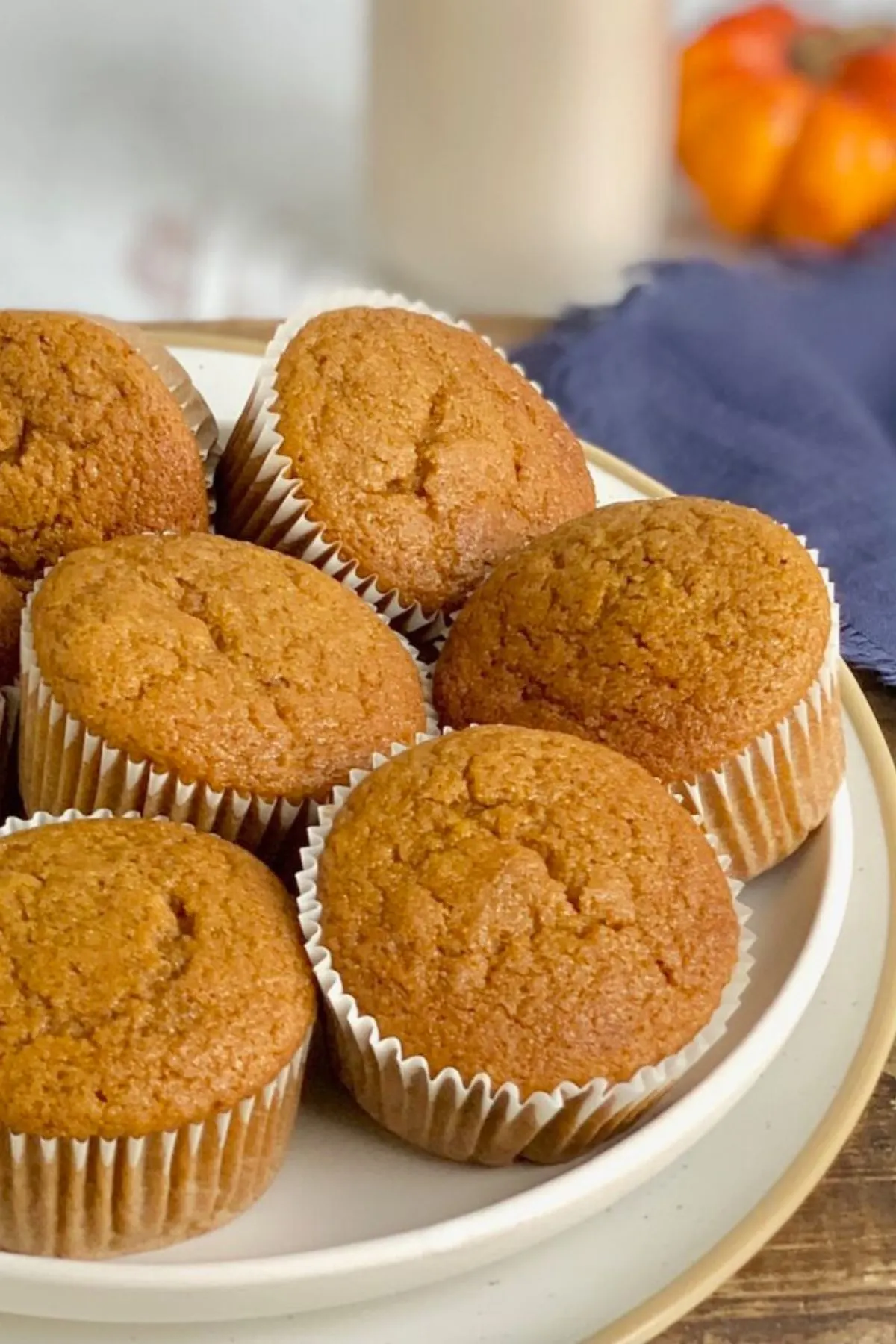 Pumpkin colored muffins in white muffins liners on a white plate across a dark serving platter.