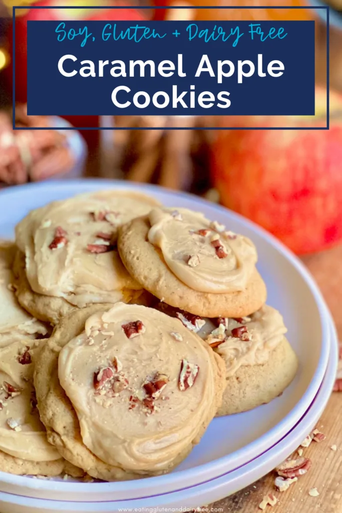 A white plate full of small golden colored cookies with a brown frosting on top and chopped nuts next to a jar of cinnamon sticks.