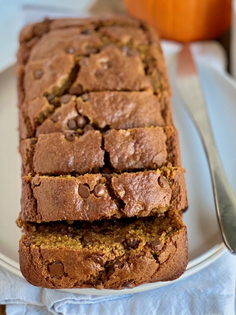 A large loaf of golden colored quick bread with large slices and chocolate chips in it.