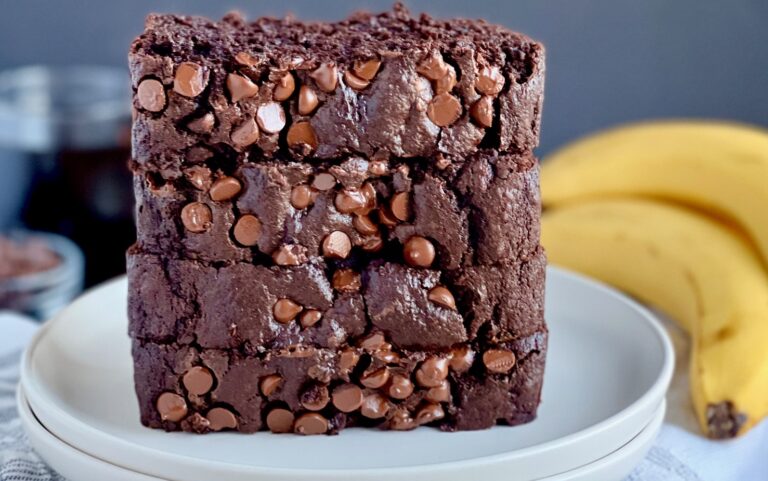 A white plate holding thick slices of dark brown bread with lots of chocolate chips.