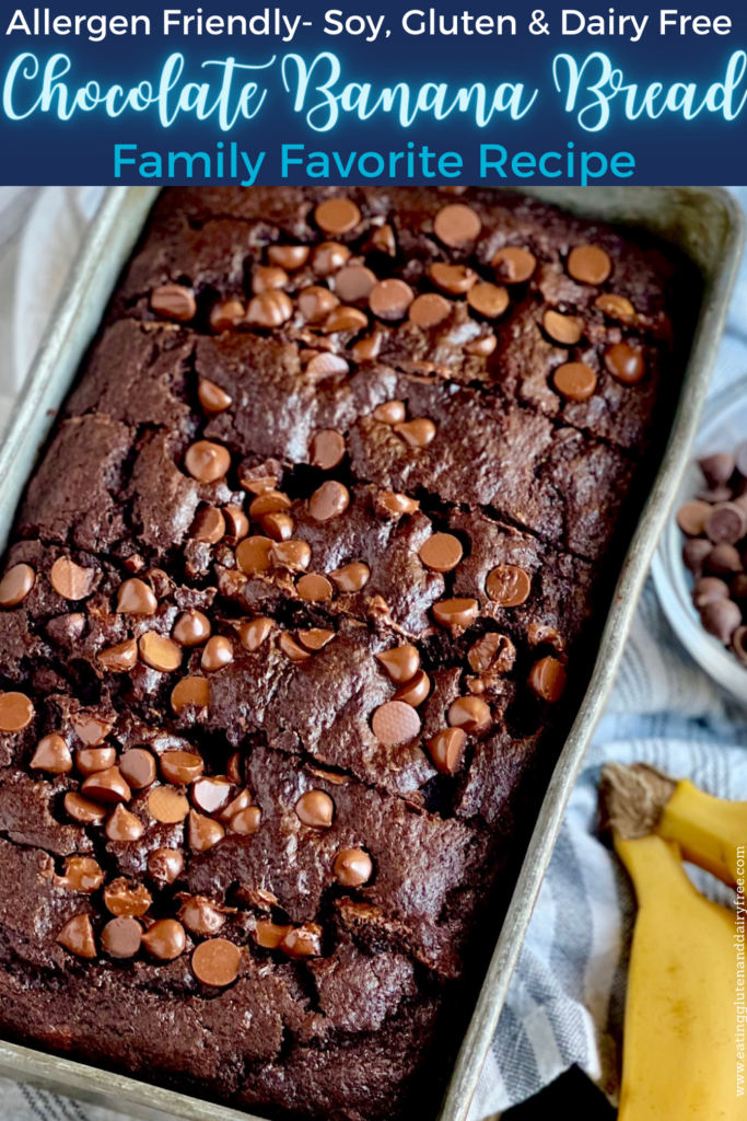 A metal loaf pan with a dark brown bread in it and chocolate chips on top. You can also see 2 bananas next to the loaf pan