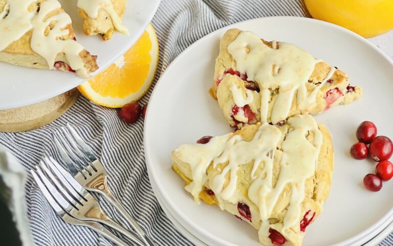 2 light colored triangle shaped scones with pops of red cranberries. Topped with a light orange colored glaze drizzled across the top.