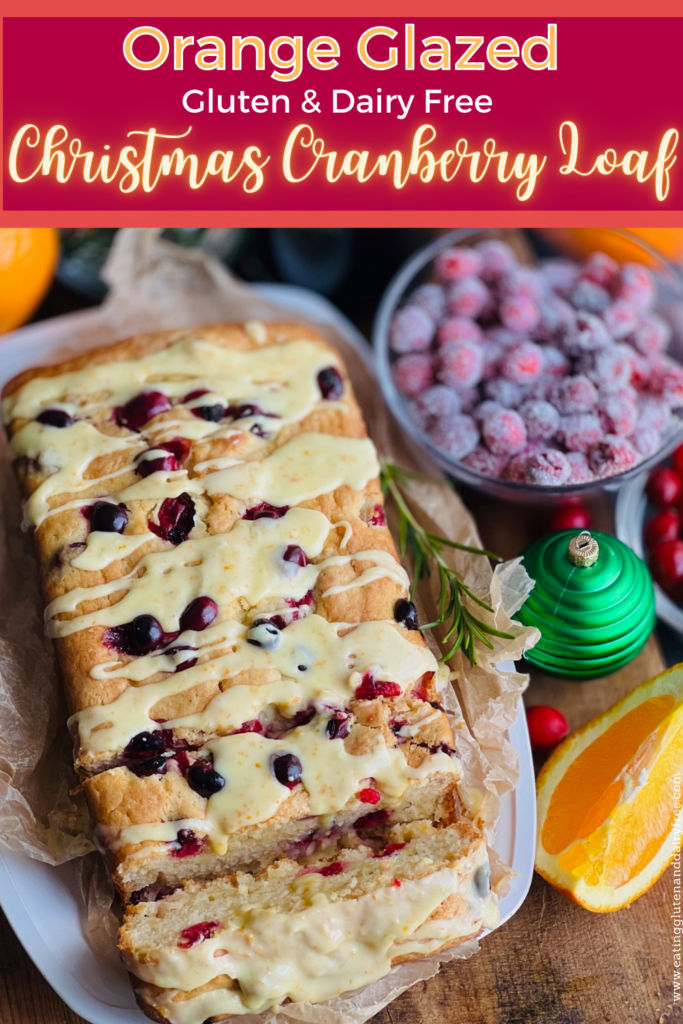 A white bread dish with a cream colored rectangle loaf  that has been cut into slices with red circle cranberries popping out of the bread. A light orange colored glaze is drizzled over the top.